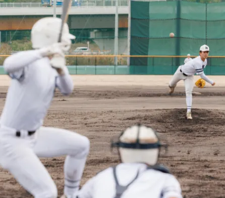 野球部の試合で、投手が全力でボールを投げ、チームでプレーに取り組んでいる部活動の様子