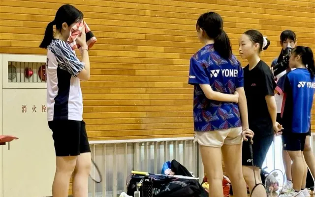 屋内の体育館で、バドミントン部の部員が集合している様子