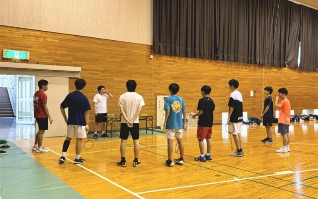 屋内の体育館で、バドミントン部の部員が説明を聞いている様子