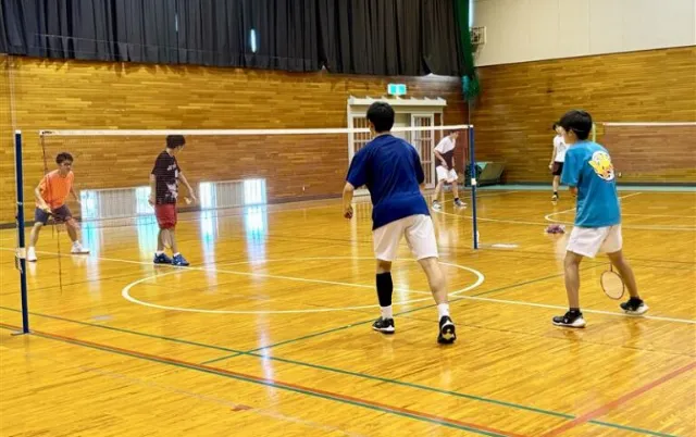 屋内の体育館で、バドミントン部の部員がシャトルを打っている様子