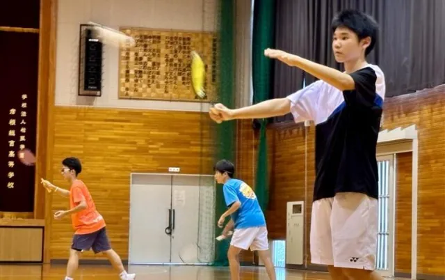 屋内の体育館で、バドミントン部の部員がシャトルを打ち返している様子