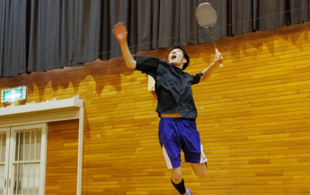 屋内の体育館で、バドミントン部の部員がスマッシュを打つ様子