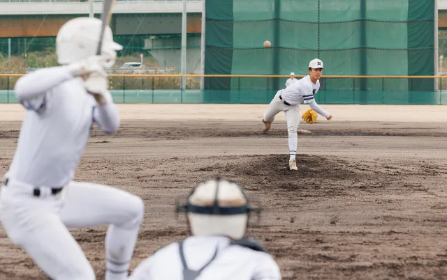 野球場で、投手と打者、捕手が構えてプレーしている様子