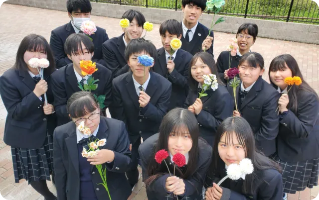 吹奏楽部の部員が花を手に持ち、集合写真を撮影している様子