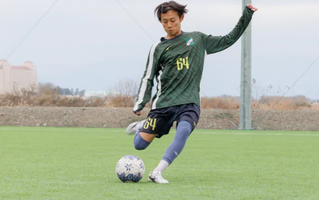 サッカー部の部員が屋外グラウンドでシュート動作をしている様子