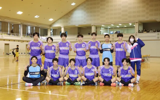 屋内の体育館で、ハンドボール部の部員が集合している様子