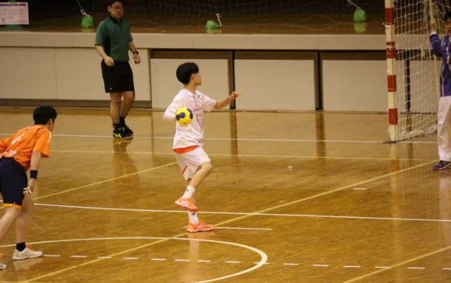 屋内の体育館で、ハンドボール部の部員が試合形式で動いている様子