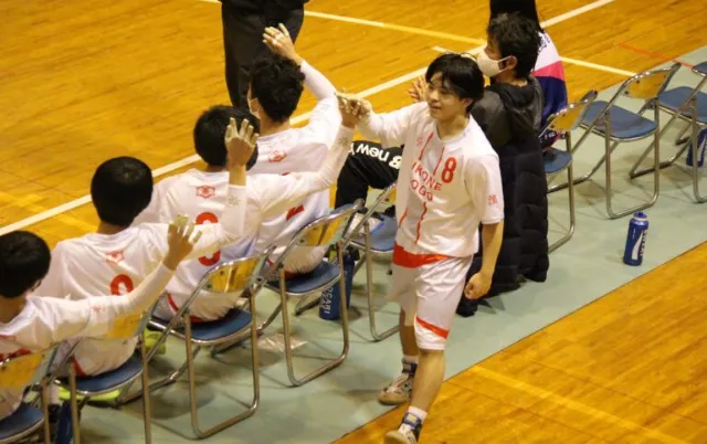 屋内の体育館で、ハンドボール部の部員がジャンプしてプレーしている様子