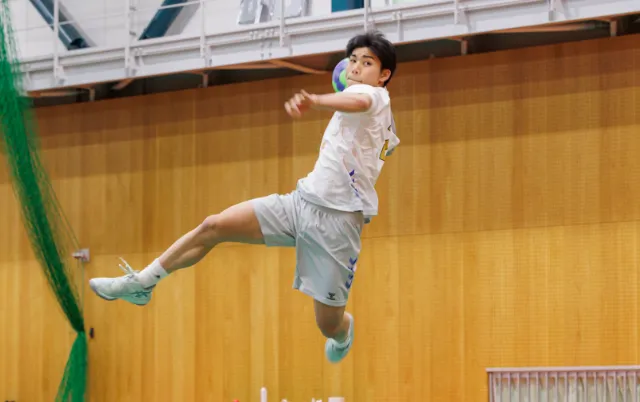 屋内の体育館で、ハンドボール部の部員がボールを投げる動作をしている様子