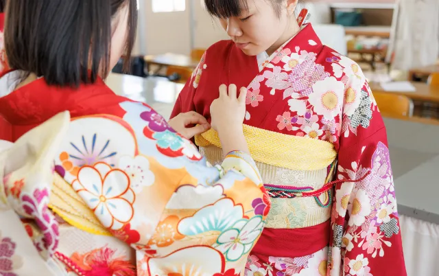 赤い浴衣を着た部員が帯の結び方を確認している様子