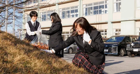 屋外で、生徒たちが手袋を着用して草や落ち葉を回収している活動の様子